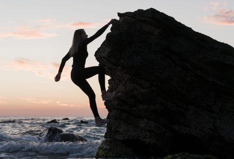 long-shot-woman-climbing-rock-next-to-the-ocean