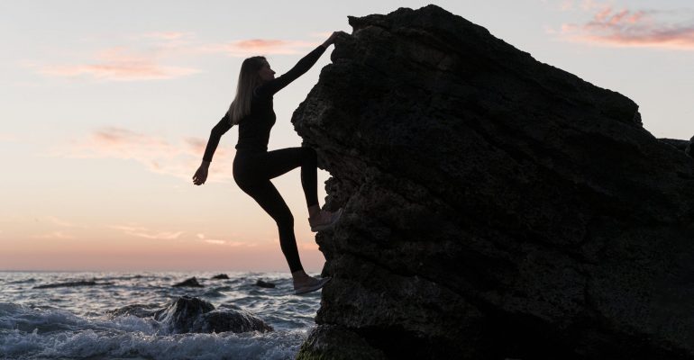 long-shot-woman-climbing-rock-next-to-the-ocean